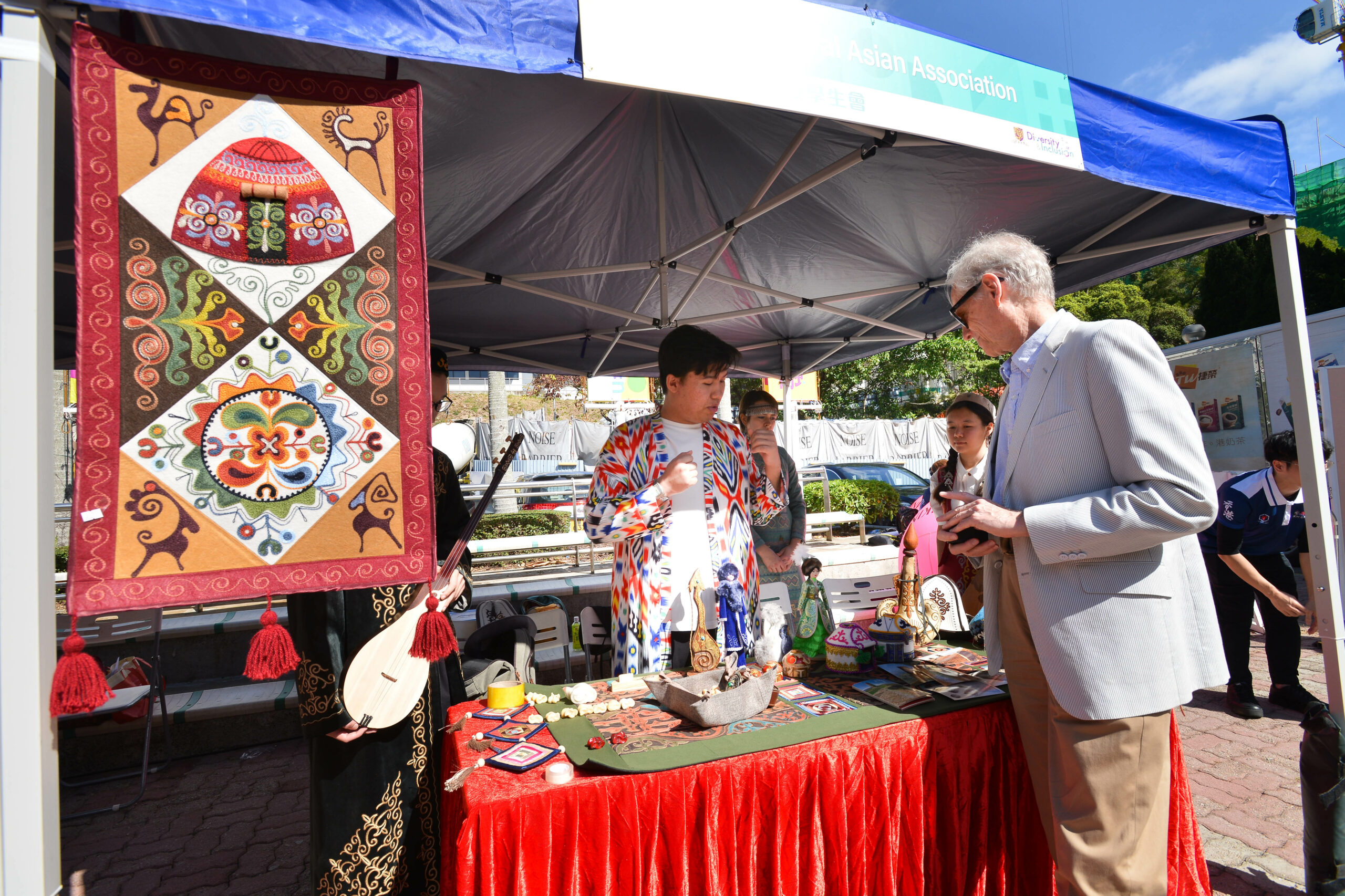 A booth under a blue canopy tent, featuring traditional items like a colorful tapestry, musical instruments, and handcrafted items.