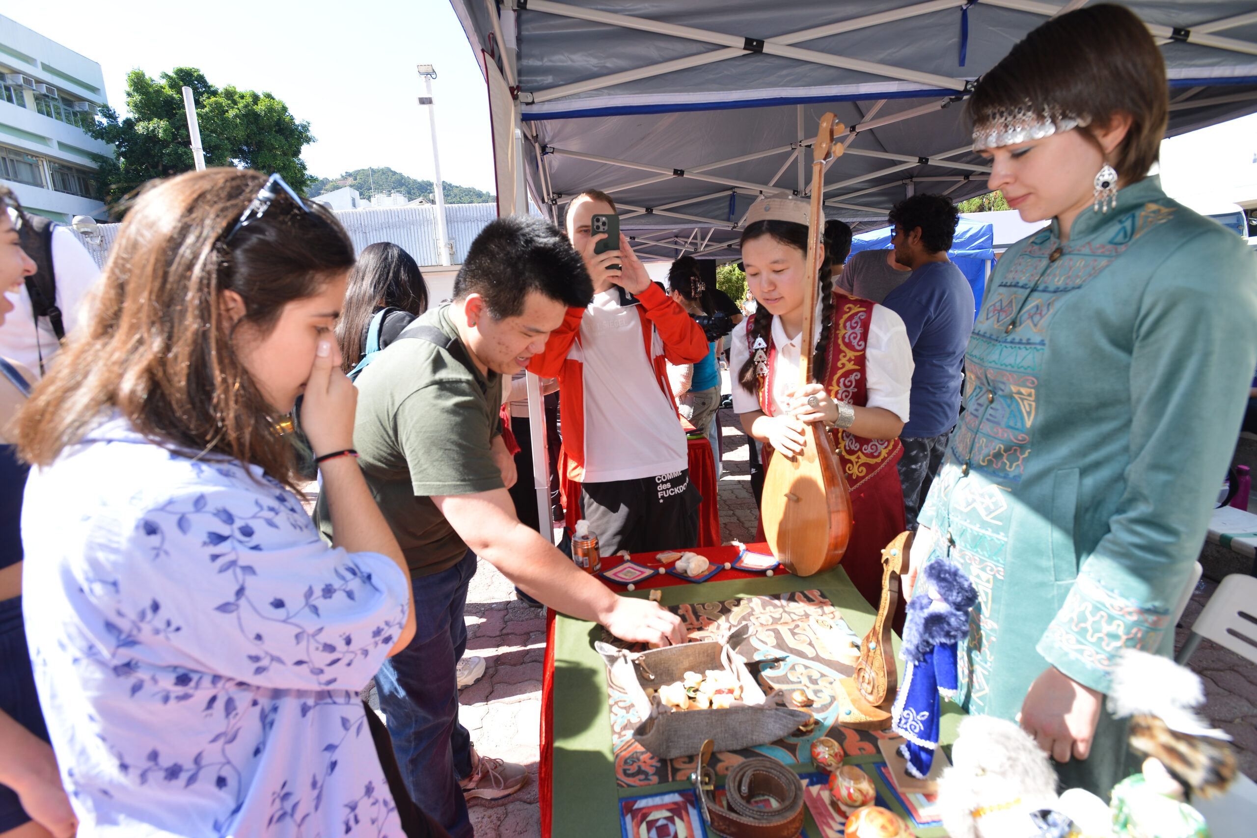 Two students from Central Asian Student Association displaying cultural artifacts and musical instruments at an outdoor event under a canopy