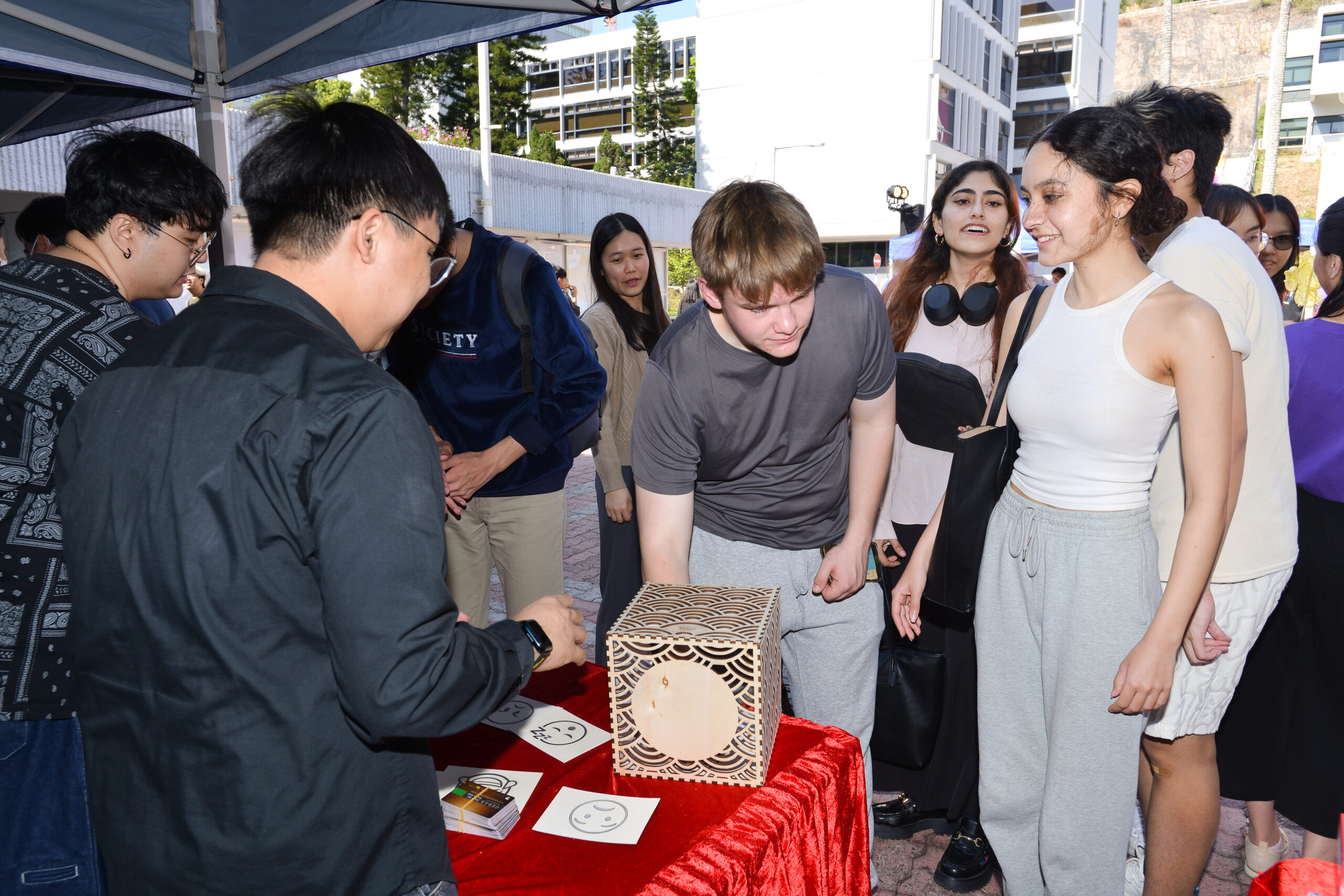 Participants at D&I Carnival 2024 gathered around a table under a tent with a decorative box and cards with smiley faces.