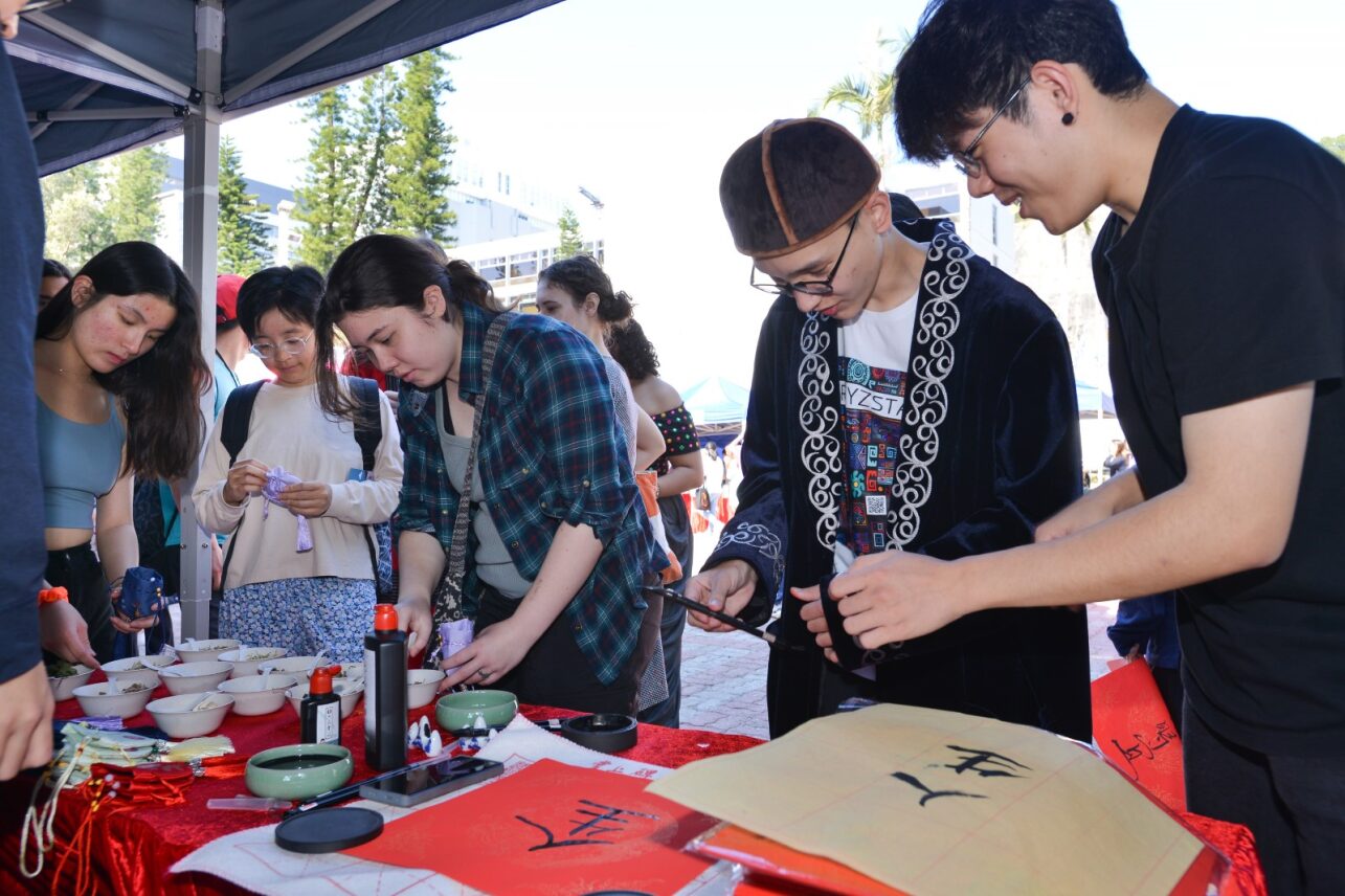 Participants at D&I Carnival 2024, engaged in writing fai chuns under a canopy tent.