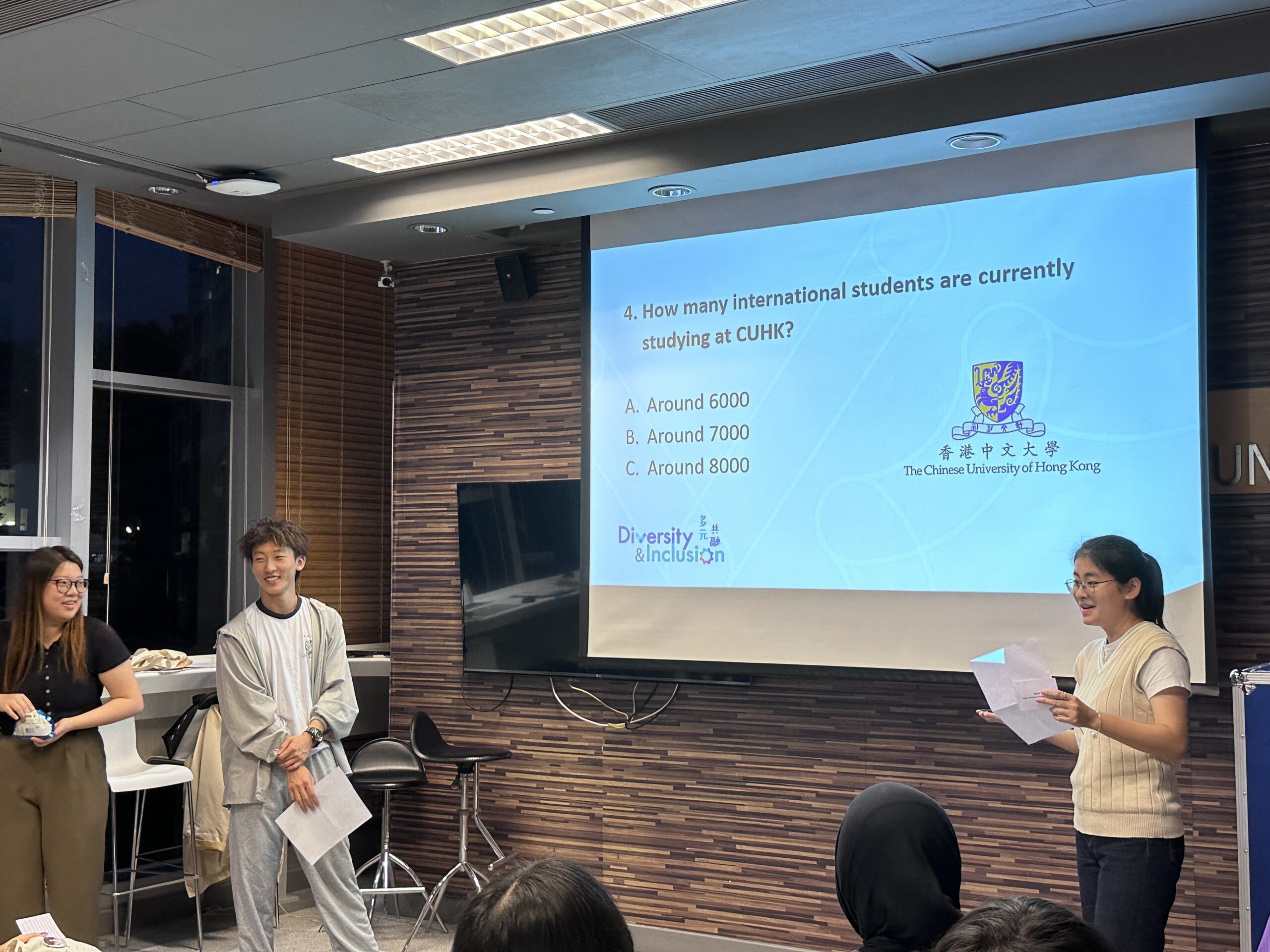 A group of people wearing purple "Diversity & Inclusion" shirts are playing the CUHK Q&A game at the D&I Ambassador Programme Closing Ceremony. They stand in front of a screen displaying a question, engaging in the Q&A activity.