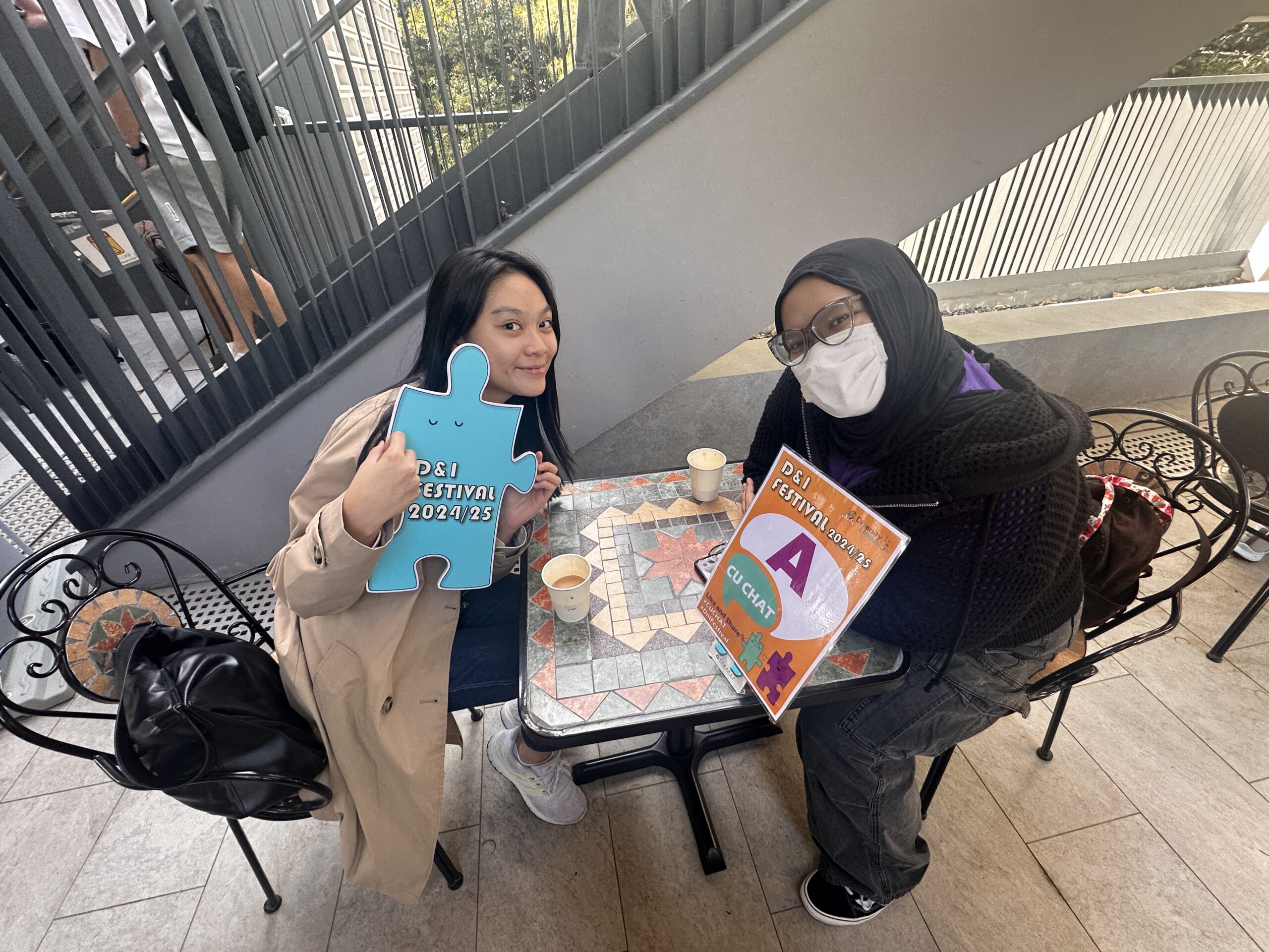 The D&I ambassador and a participant are holding colorful props promoting D&I festivals, smiling.